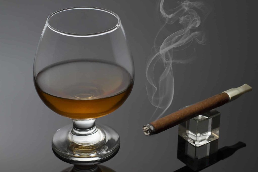 a picture depicting a glass of whiskey with a lit cigar next to it